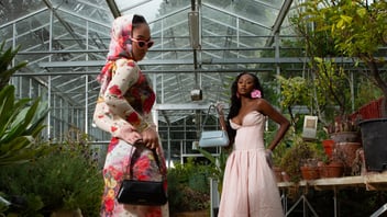 two people in dresses, one with a handbag, inside a green house with plants