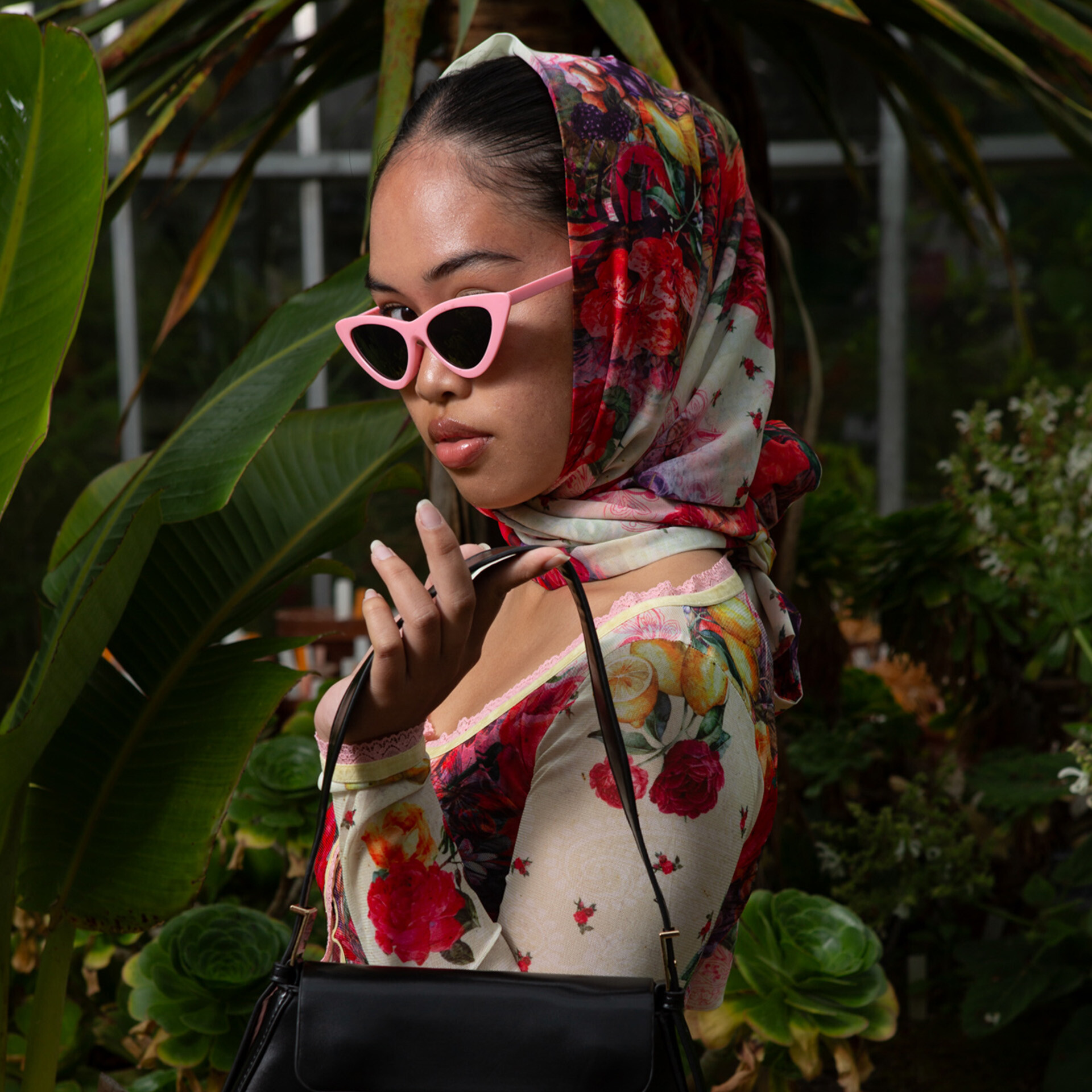 a person wearing sunglasses holding a handbag in a greenhouse