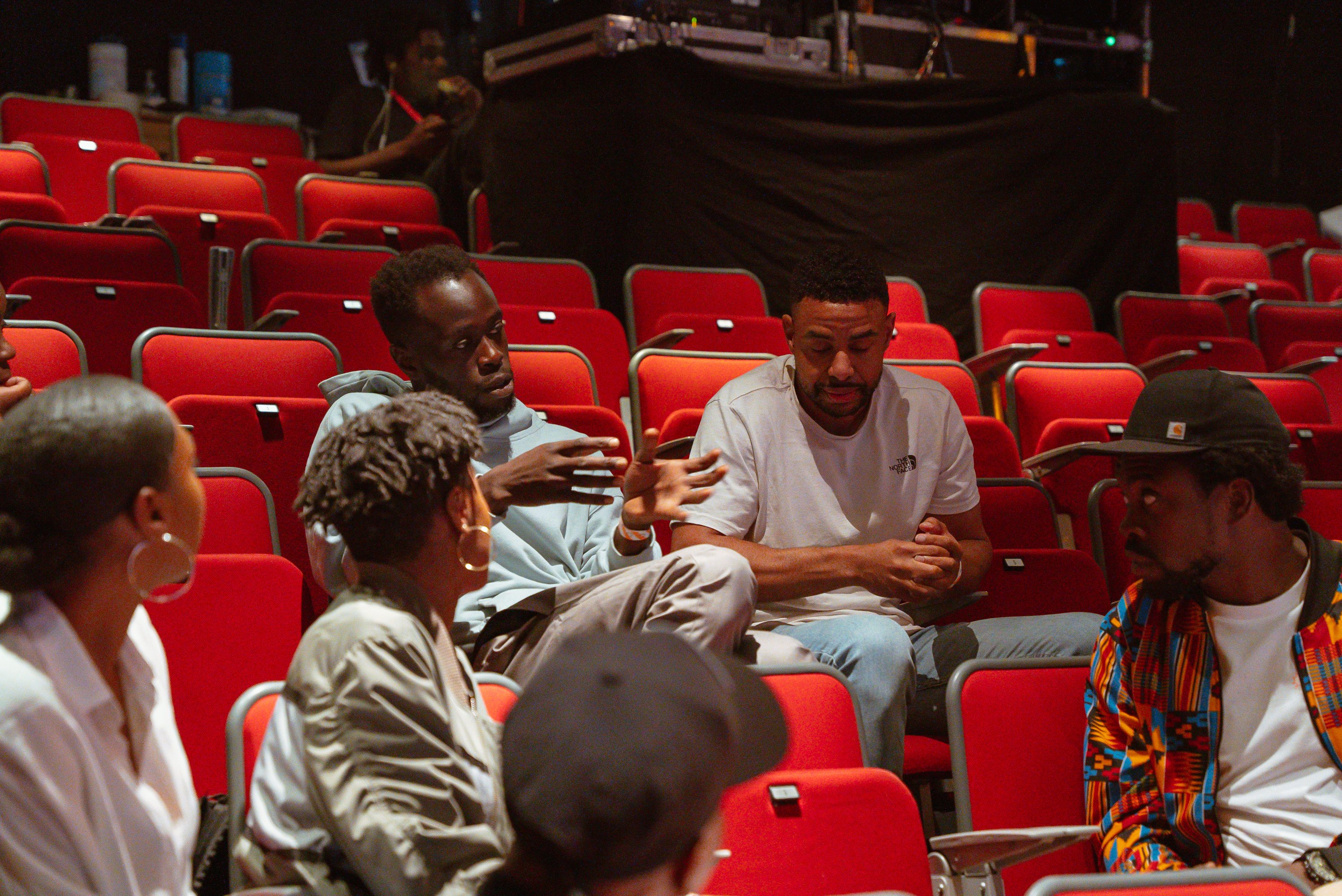 a group of people having a conversation sitting on red chairs