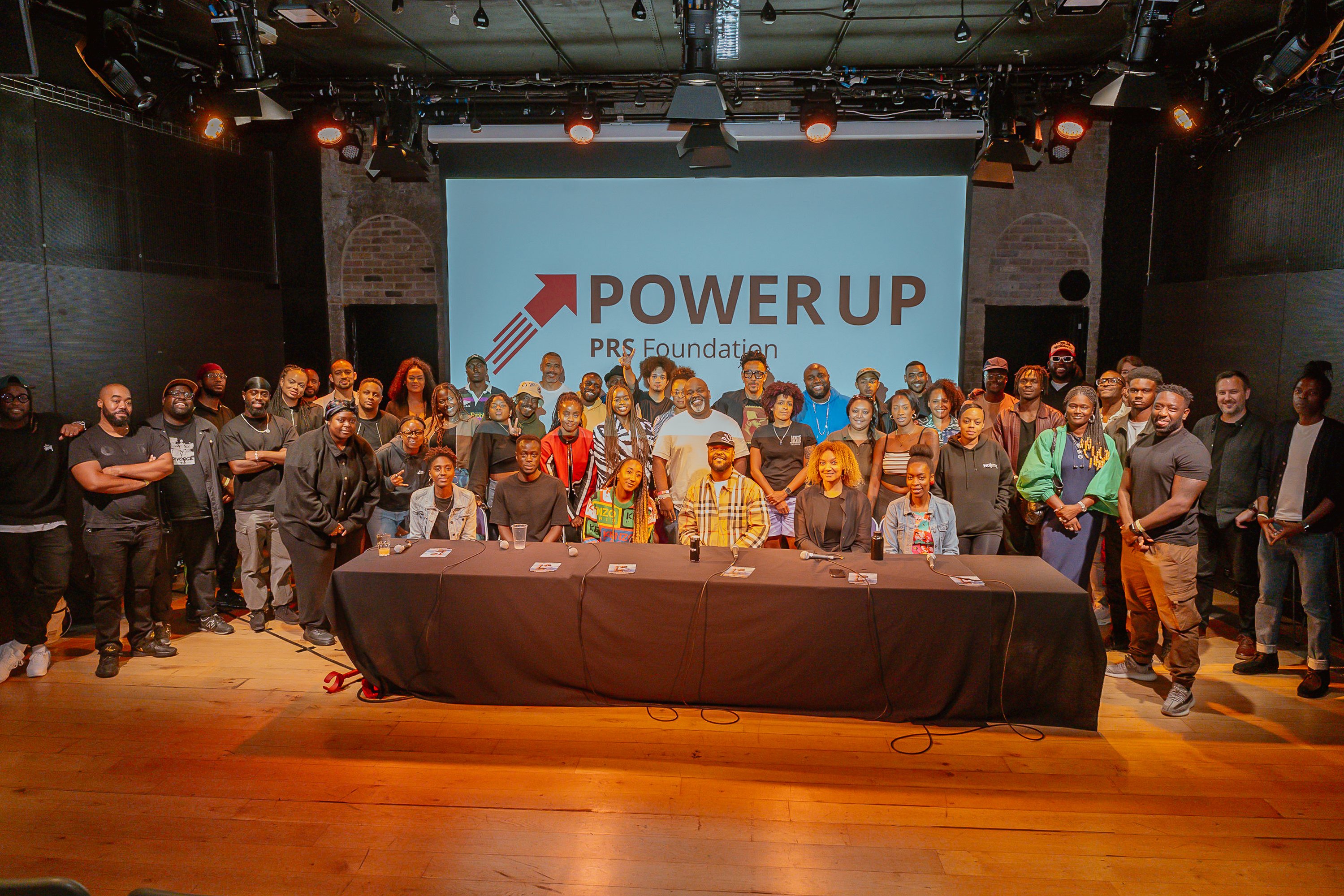 a room full of people in front of an image saying "POWER UP PRS Foundation"