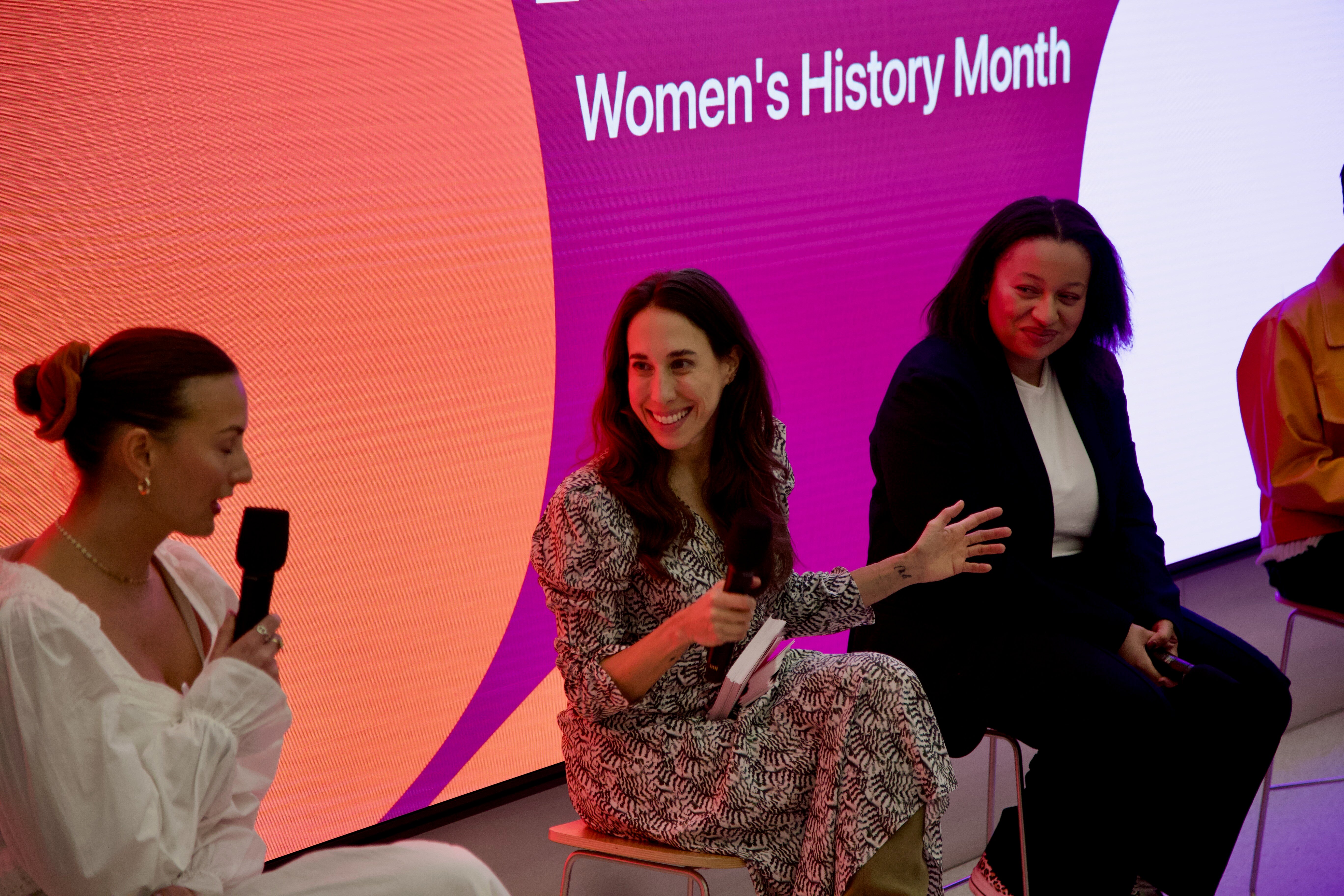 three panellists on a stage in front of an LED display that says "Women's History Month"