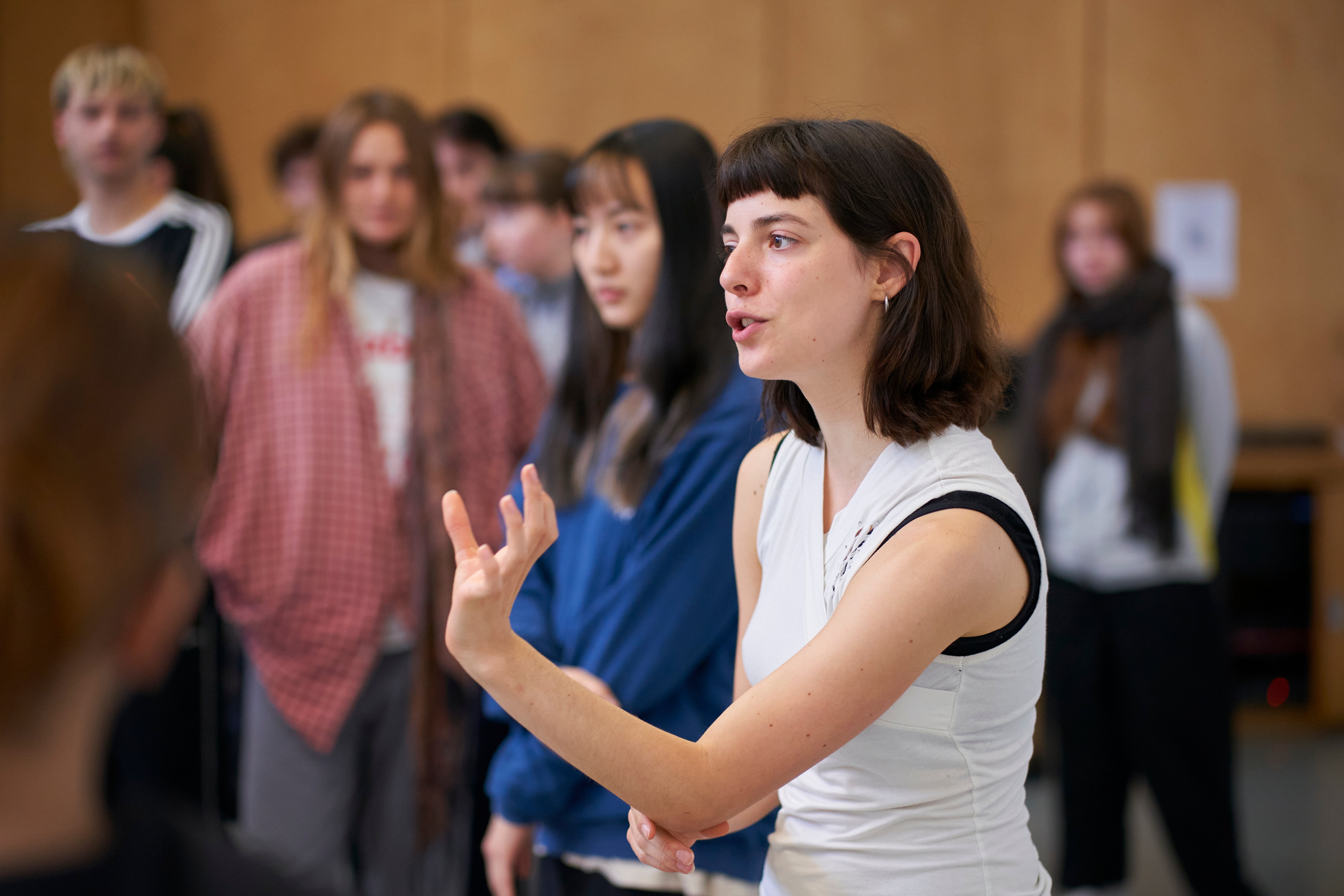 a room full of people standing in a rehearsal space, listening to one person explain something