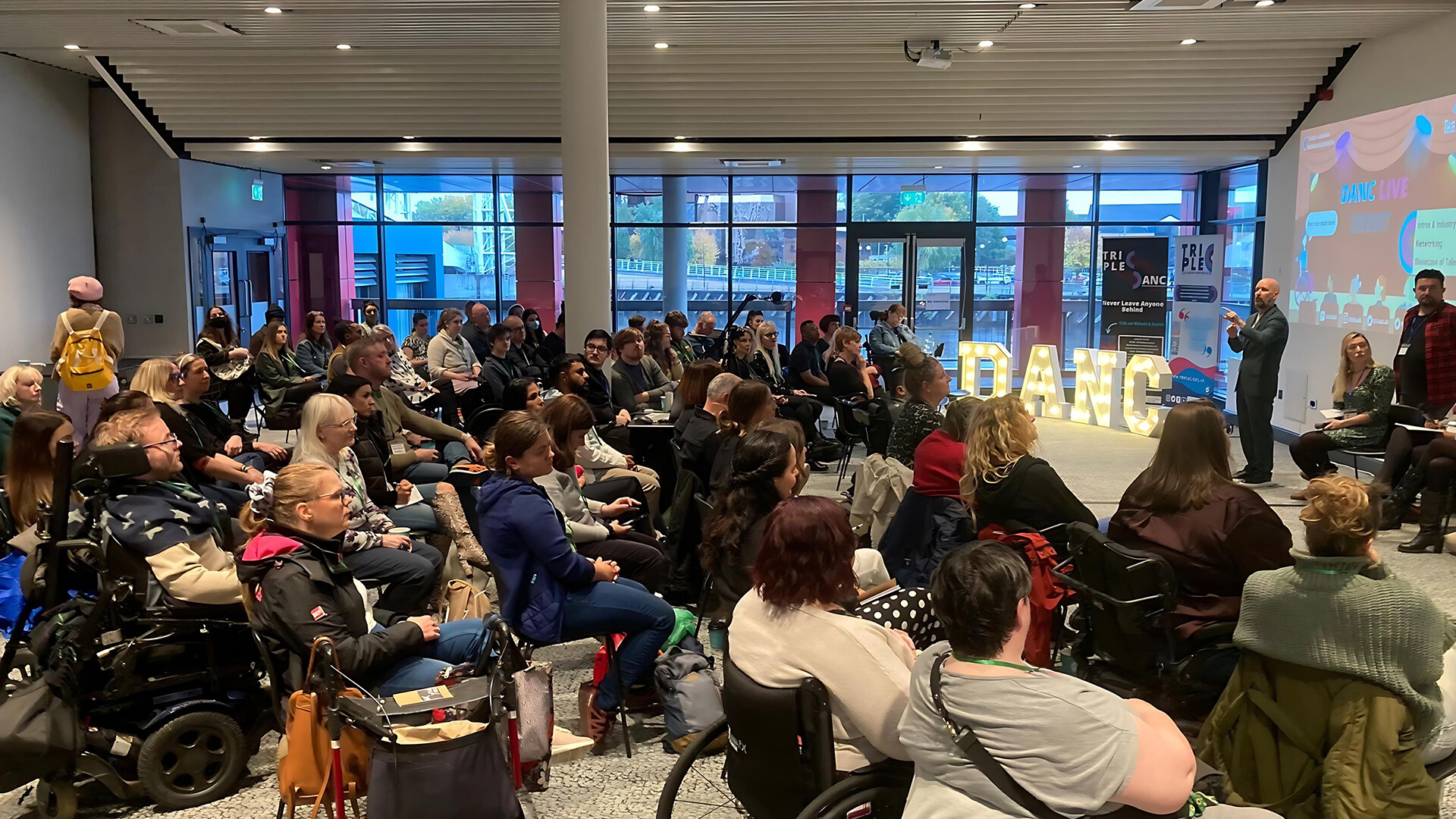 a room full of people including wheelchair users, watching a presentation about DANC