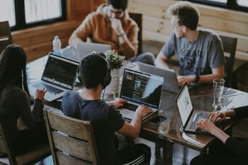 four people on a desk, working on laptops