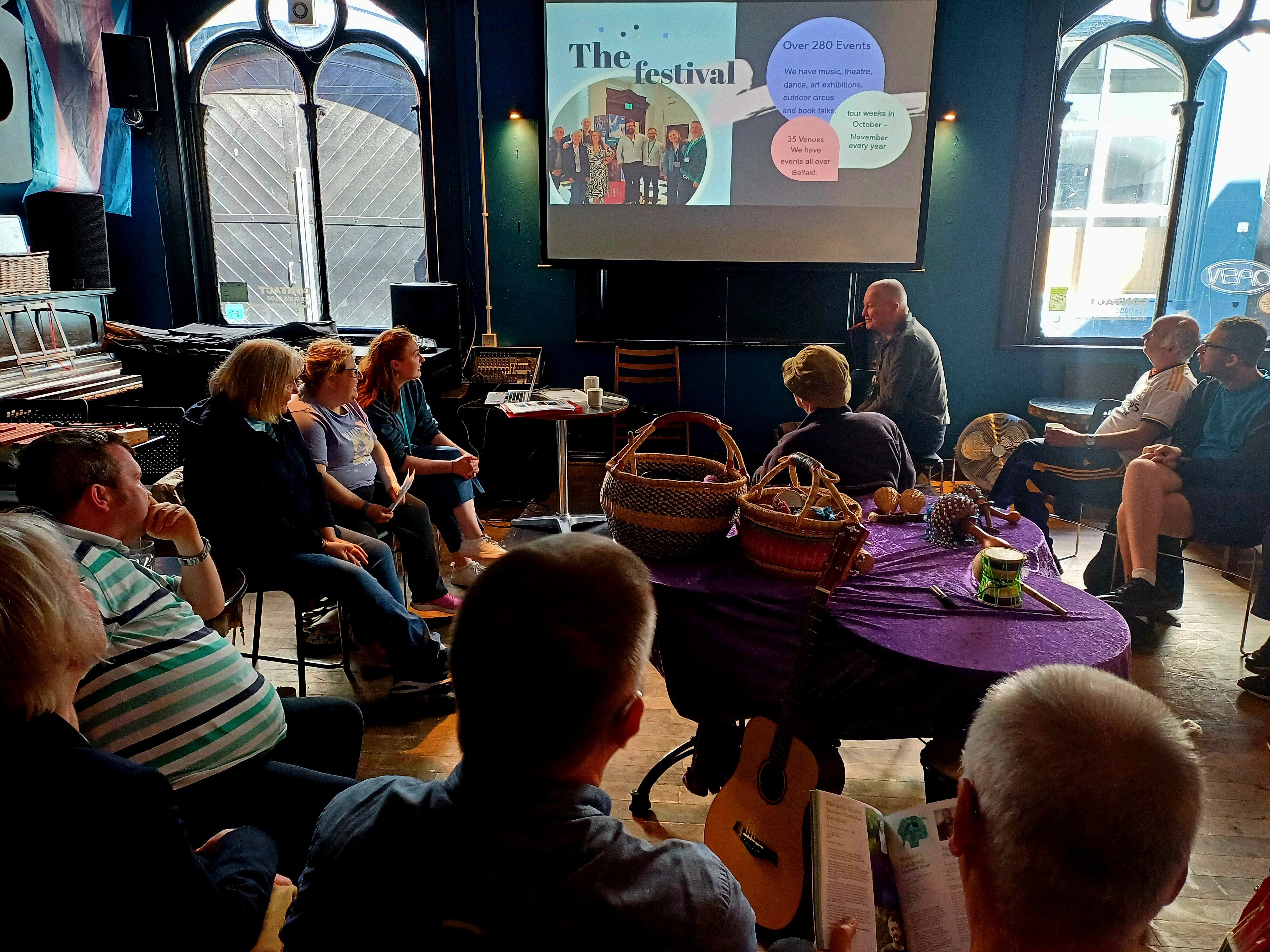 a meeting of people planning, with a projector slide saying "the festival"