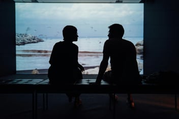 two people sitting on a bench watching an exhibit