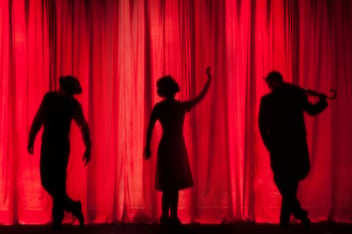 the silhouettes of three actors on a stage against a red curtain